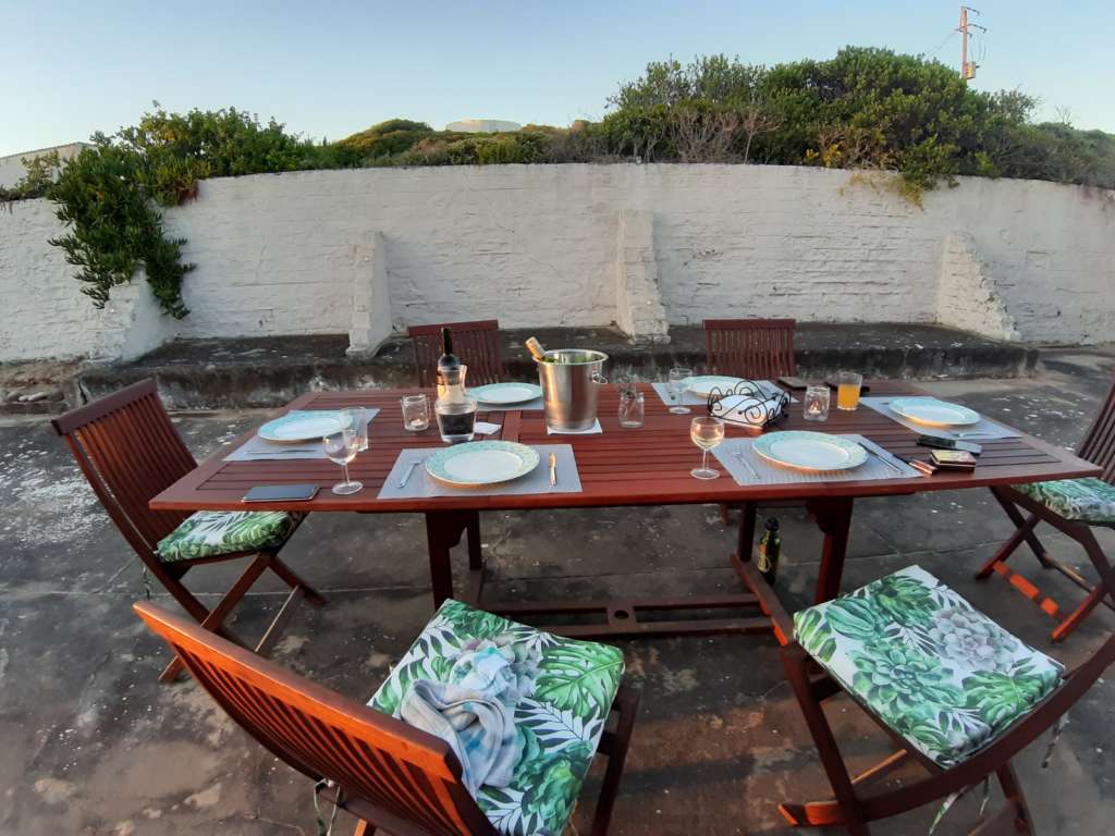 'n Teak-buitelug-eettafel met tafelinstellings, stoele en kussings, naby die braai op Fonteintjies.