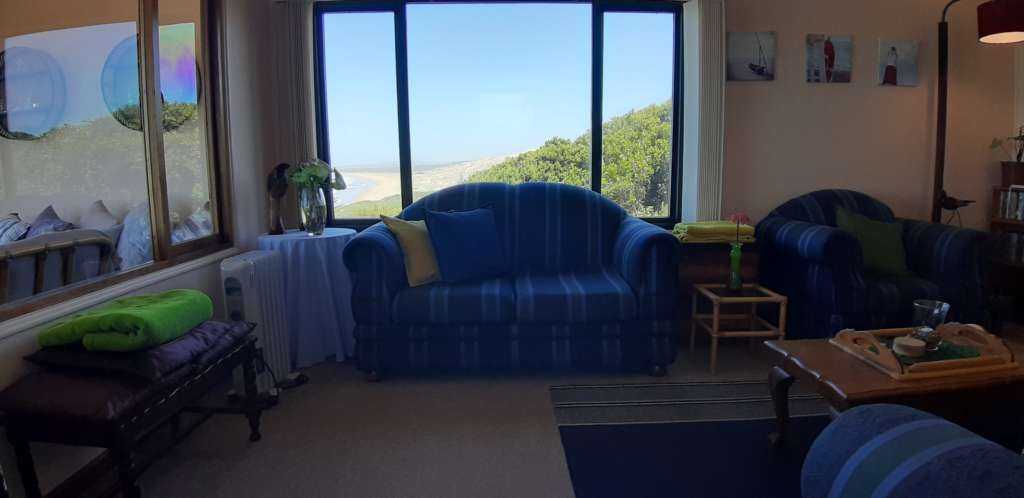 Die Lounge im Fonteintjies. Hinter einer großen blau gestreiften Couch ist ein Fenster mit dem Meer in der Ferne sichtbar. Links ist ein Fenster, das die Lounge vom Wintergarten trennt.