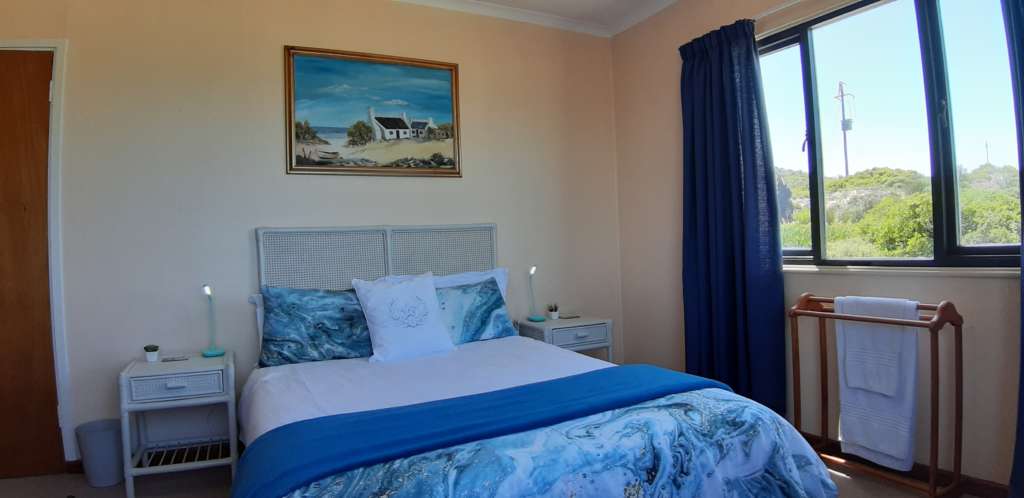 Slaapkamer 1 by Fonteintjies. Daar is 'n dubbelbed met 'n wit kopstuk. Bo die bed is 'n olieverfskildery van 'n seekothuis. Daar is bedkassies met lampe aan beide die linker- en regterkant van die bed. Daar is 'n venster in die muur aan die regterkant, en 'n deur in die verste linkerhoek.