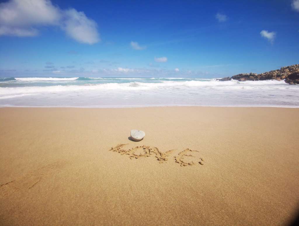 Le mot AMOUR écrit dans le sable sur une plage, avec l'océan en arrière-plan.