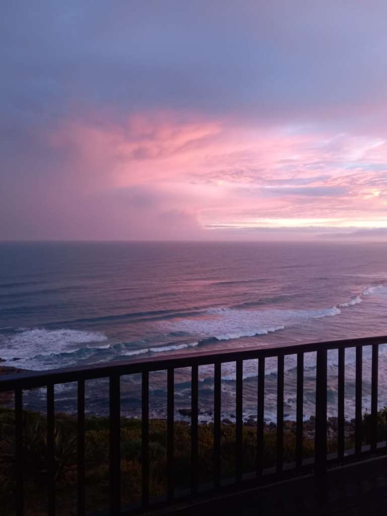 Une vue sur la mer depuis le pont du Fonteintjies. Le ciel est de plusieurs nuances de violet au coucher du soleil. Le garde-corps du pont est au premier plan.